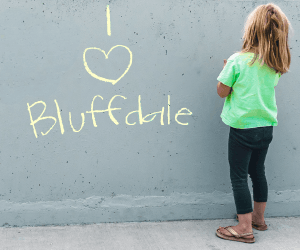 Chalk writing on wall that reads I Heart Bluffdale with small girl